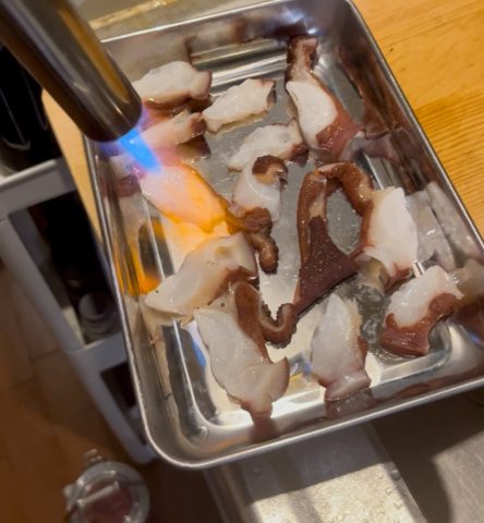 画像:タコの刺身を炙る様子。この日の肴は北海道産のタコ。バーナーで炙って旨味を凝縮します。酒がすすんでしまう